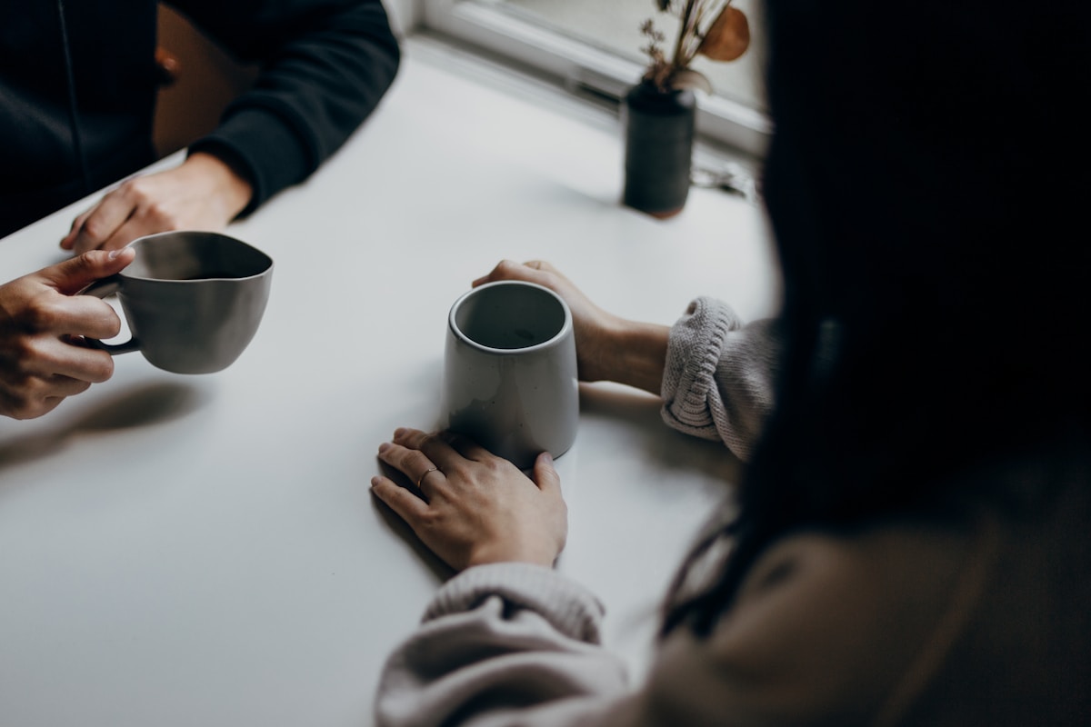 two people holding gray mugs at table