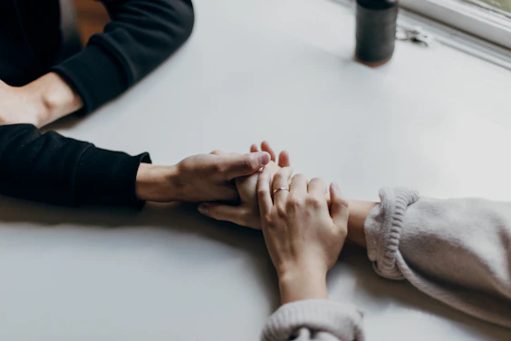 Two people holding hands on a white table, one wearing a thin ring
