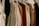 A variety of clothes hung on white plastic hangers, including sweaters, jackets, and shirts, showcasing a mix of textures like wool and cotton in neutral and earthy tones.
