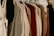 A variety of clothes hung on white plastic hangers, including sweaters, jackets, and shirts, showcasing a mix of textures like wool and cotton in neutral and earthy tones.