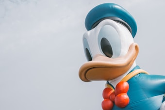 A giant inflatable sculpture of a cartoon character resembling a duck wearing a blue sailor hat and outfit with a red bow tie, positioned against a pale sky.