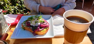 A cozy brunch table with a steaming cup of coffee and a plate of avocado toast topped with cherry tomatoes and microgreens.
