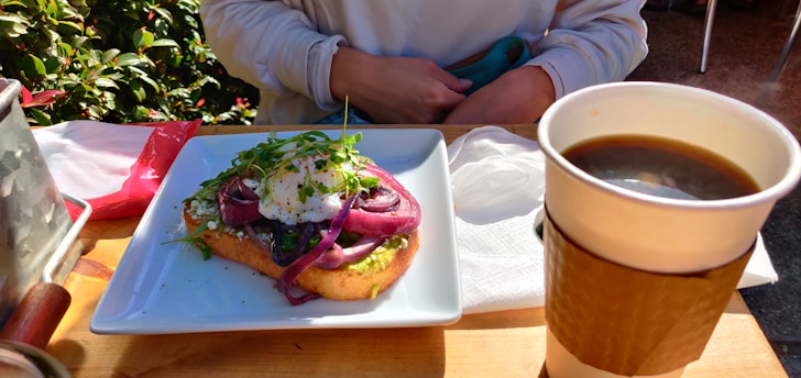 A cozy brunch table with a steaming cup of coffee and a plate of avocado toast topped with cherry tomatoes and microgreens.