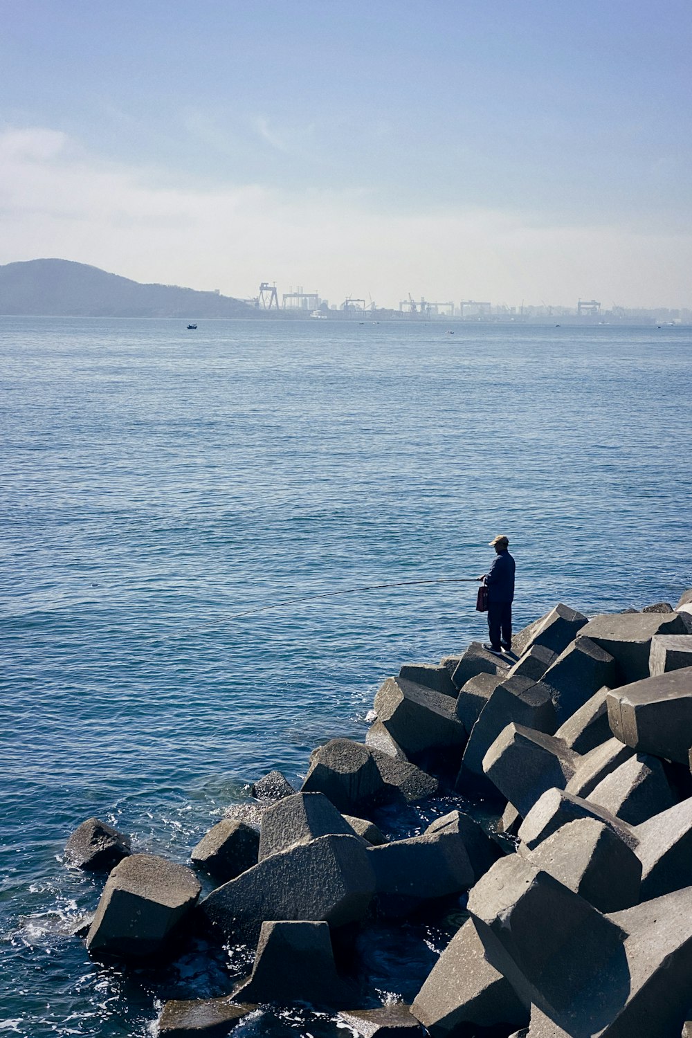 man in black jacket sitting on gray rock near body of water during daytime