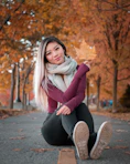 woman in purple sweater and black pants sitting on gray concrete pavement