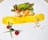 A gourmet dish is artistically presented on a white plate. Scallops, garnished with a bright orange sauce, are accompanied by a leafy green salad. A smear of vibrant yellow sauce runs across the plate, and scattered pine nuts add texture. Two red raspberries and a blueberry are positioned artfully alongside two thin green chives.