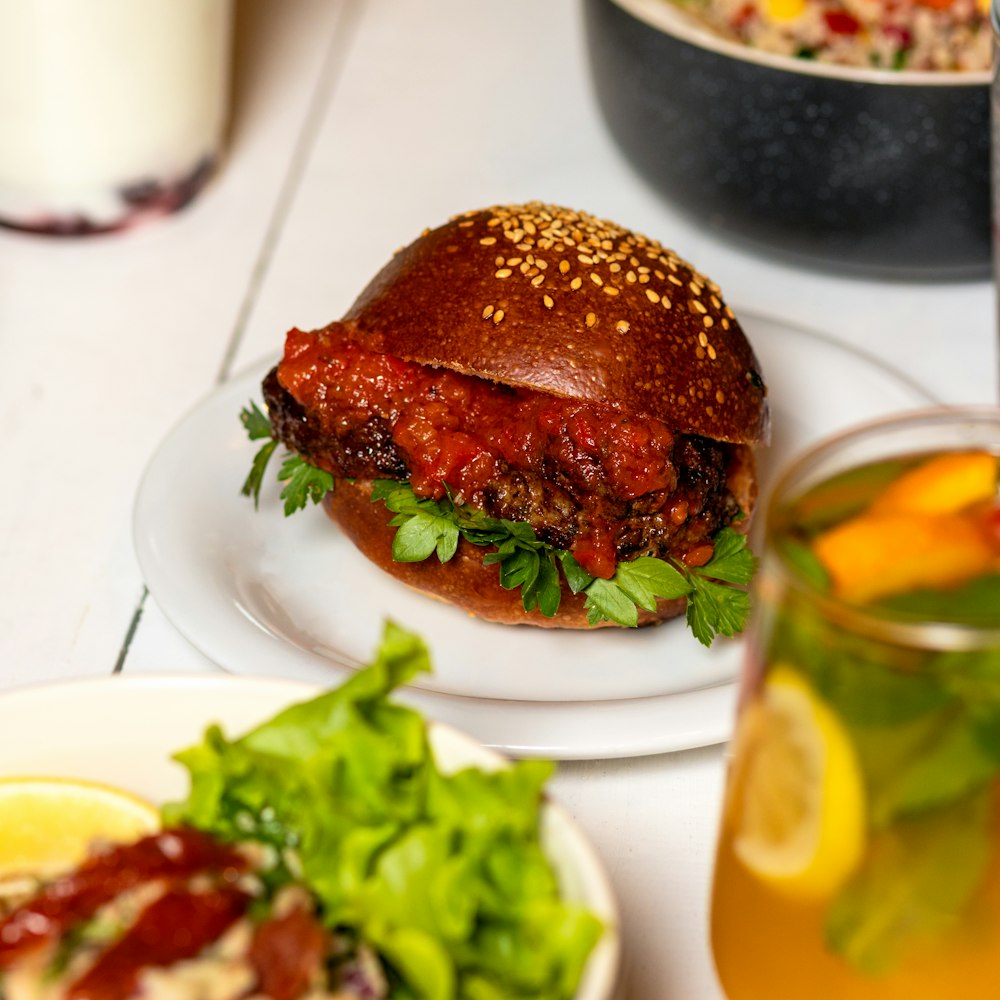 hamburguesa en plato de cerámica blanca junto a vaso transparente con líquido amarillo