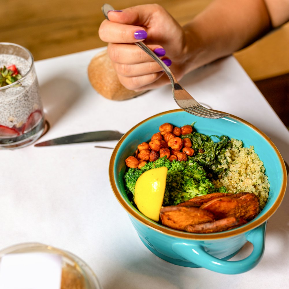 person holding spoon with food in blue ceramic bowl