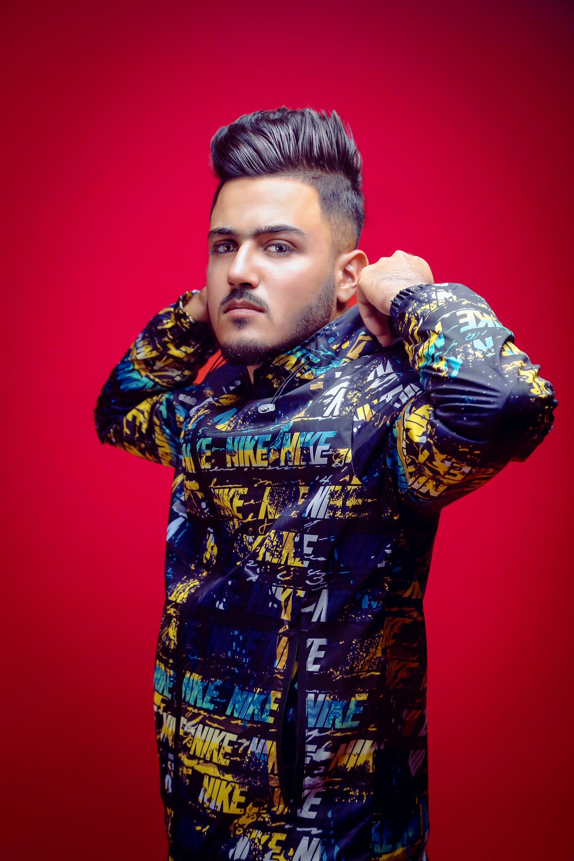 A model wearing a bright, oversized neon jacket with graffiti-style prints, standing against a colorful urban mural.