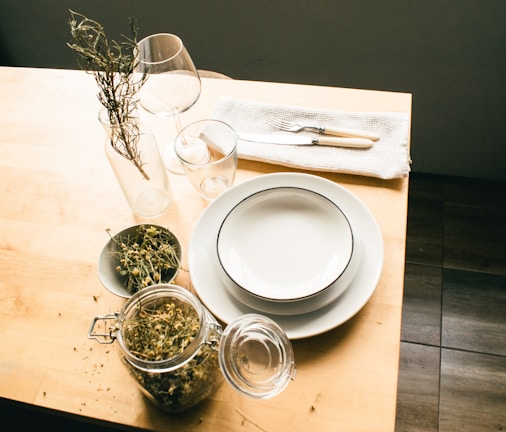 Woven jute table mats laid out on a rustic dining table with simple ceramic plates and fresh herbs.