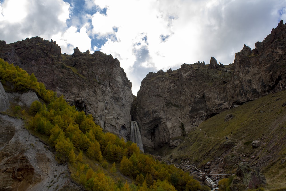 árvores verdes na montanha rochosa sob nuvens brancas durante o dia