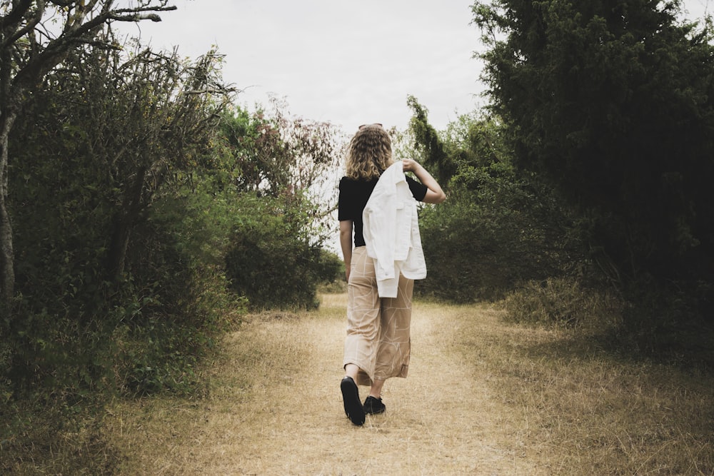 woman in white dress shirt and black pants standing on green grass field during daytime