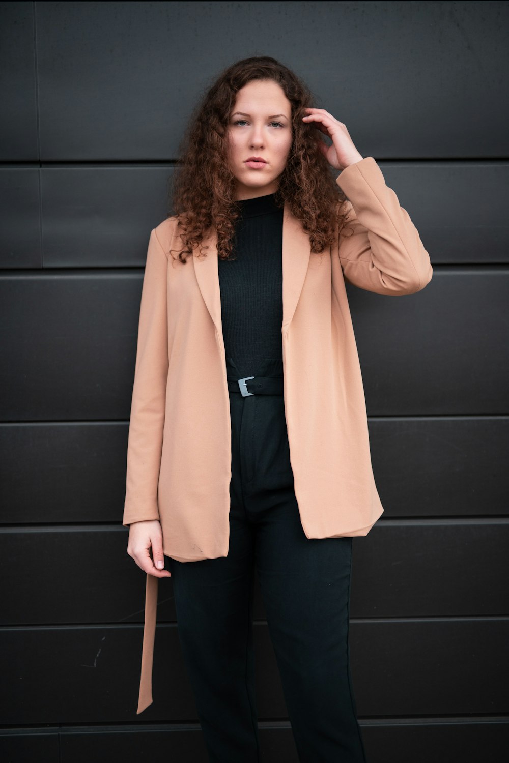 woman in beige coat standing beside black wall