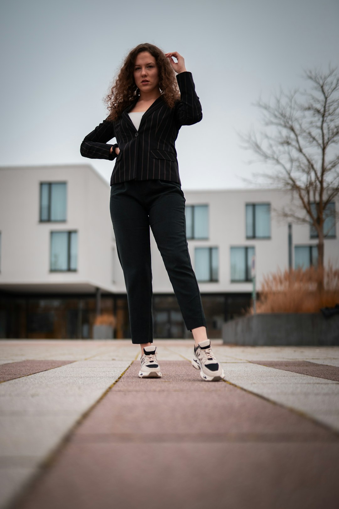 woman in black pants and white sneakers standing on gray concrete pavement during daytime