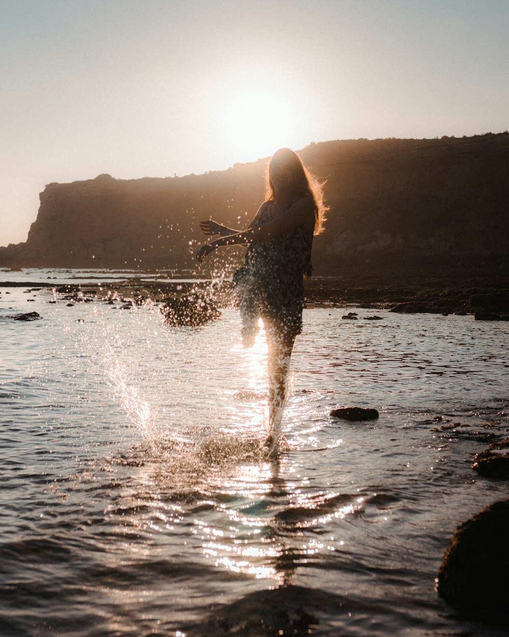 woman in black dress standing on water during sunset