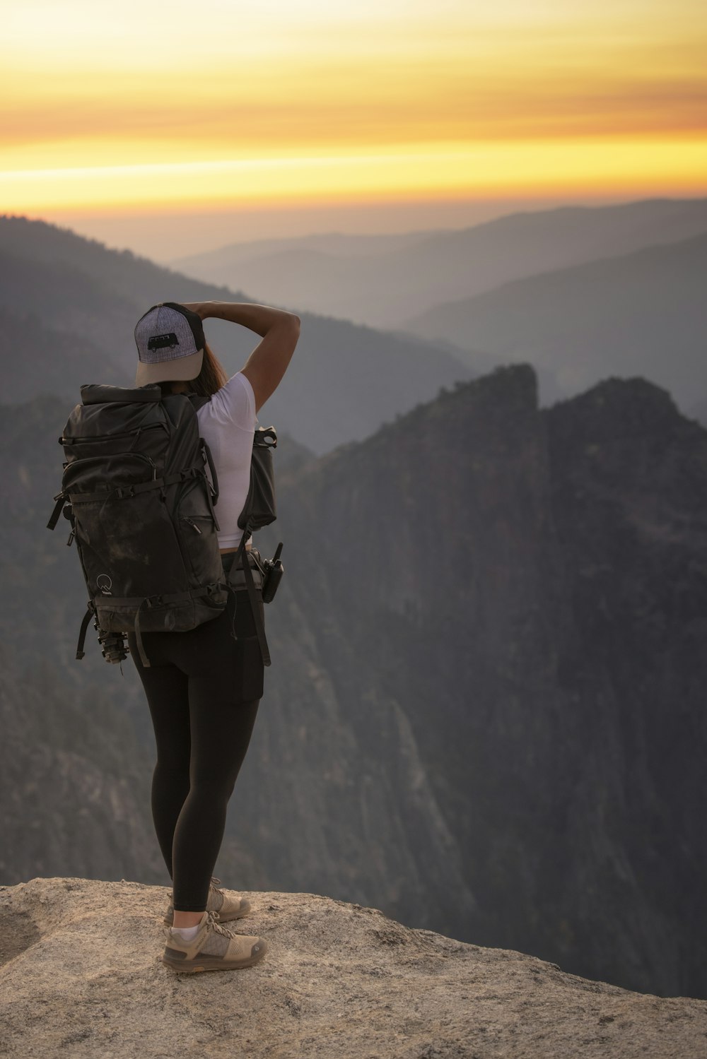 woman in black pants and black backpack standing on cliff during daytime