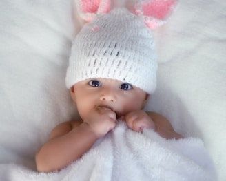 baby in white knit cap lying on white textile