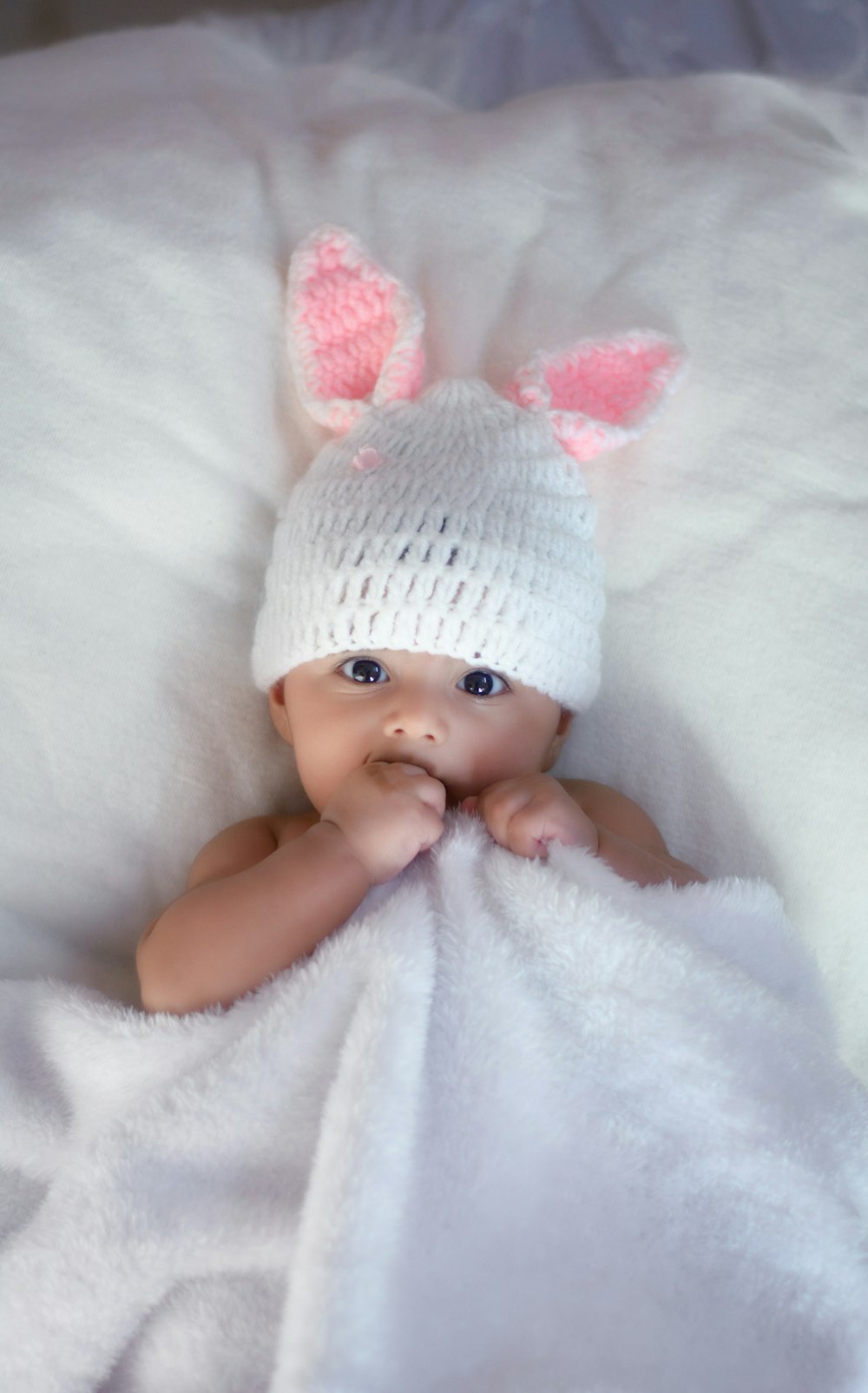 흰색 직물에 누워 있는 흰색 니트 모자를 쓴 아기
