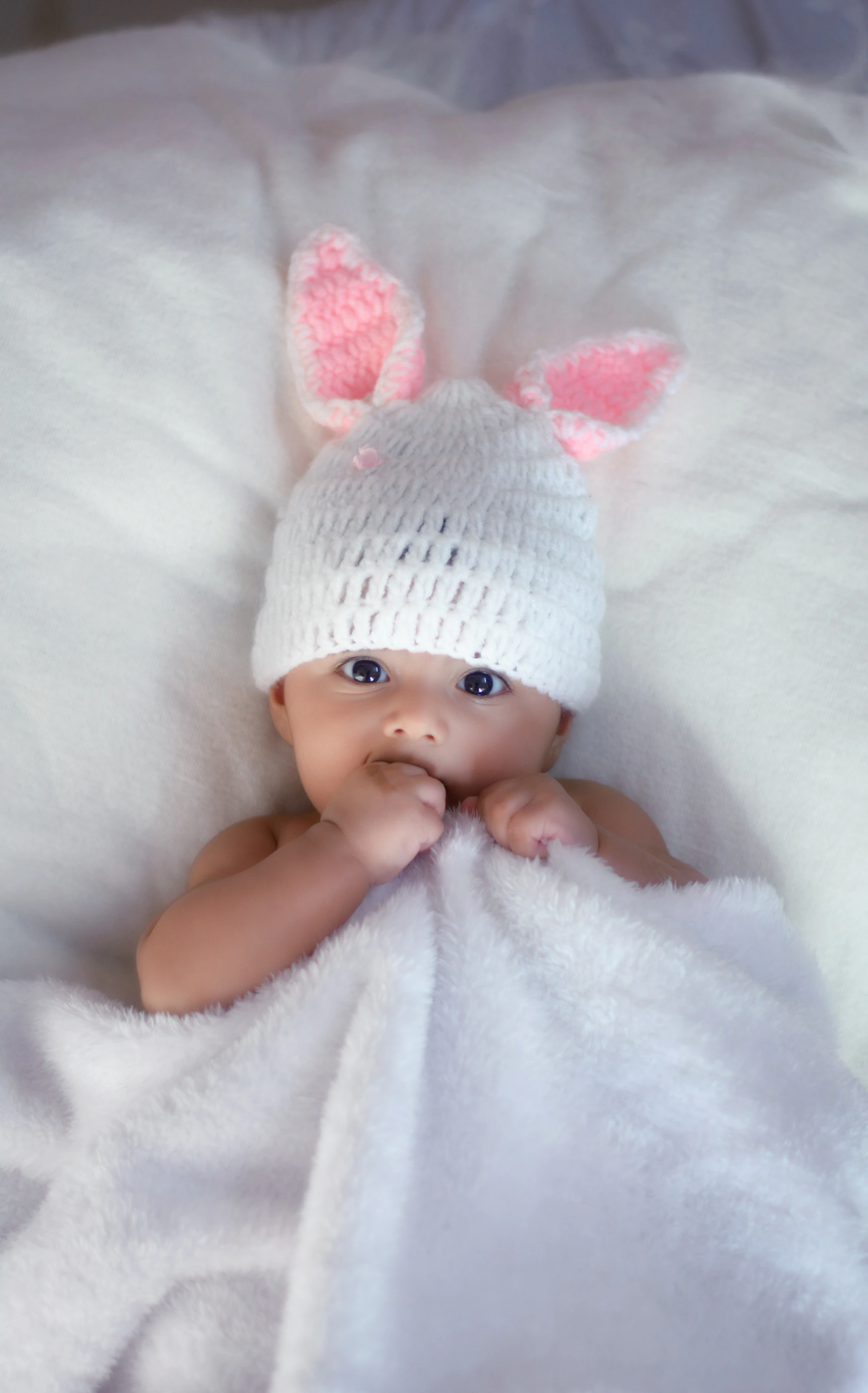 Newborn baby in a white knit cap on soft white fabric
