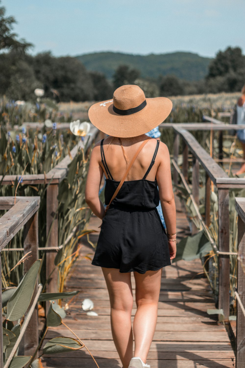 woman in black spaghetti strap dress wearing brown sun hat standing on brown wooden bridge during