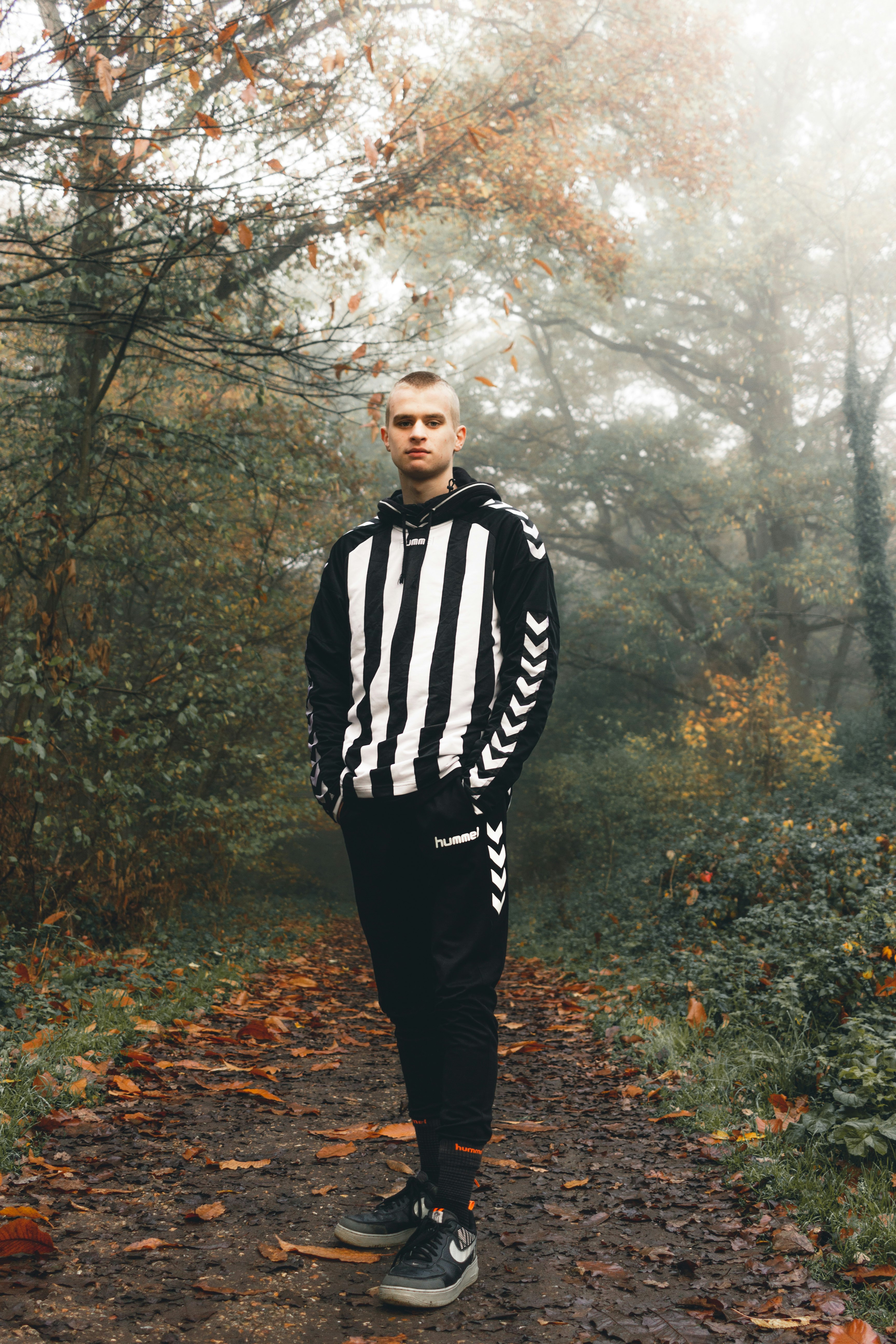 man in black and white adidas jacket standing on forest during daytime