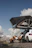 A smiling camper sitting beside a car with a rooftop tent set up under a clear blue sky.