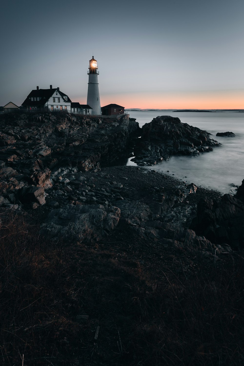 日没時の岩だらけの海岸にある白と黒の灯台