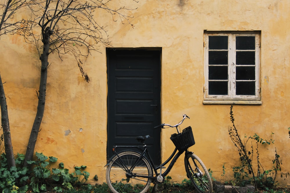 bicicleta da cidade preta estacionada ao lado da porta de madeira preta