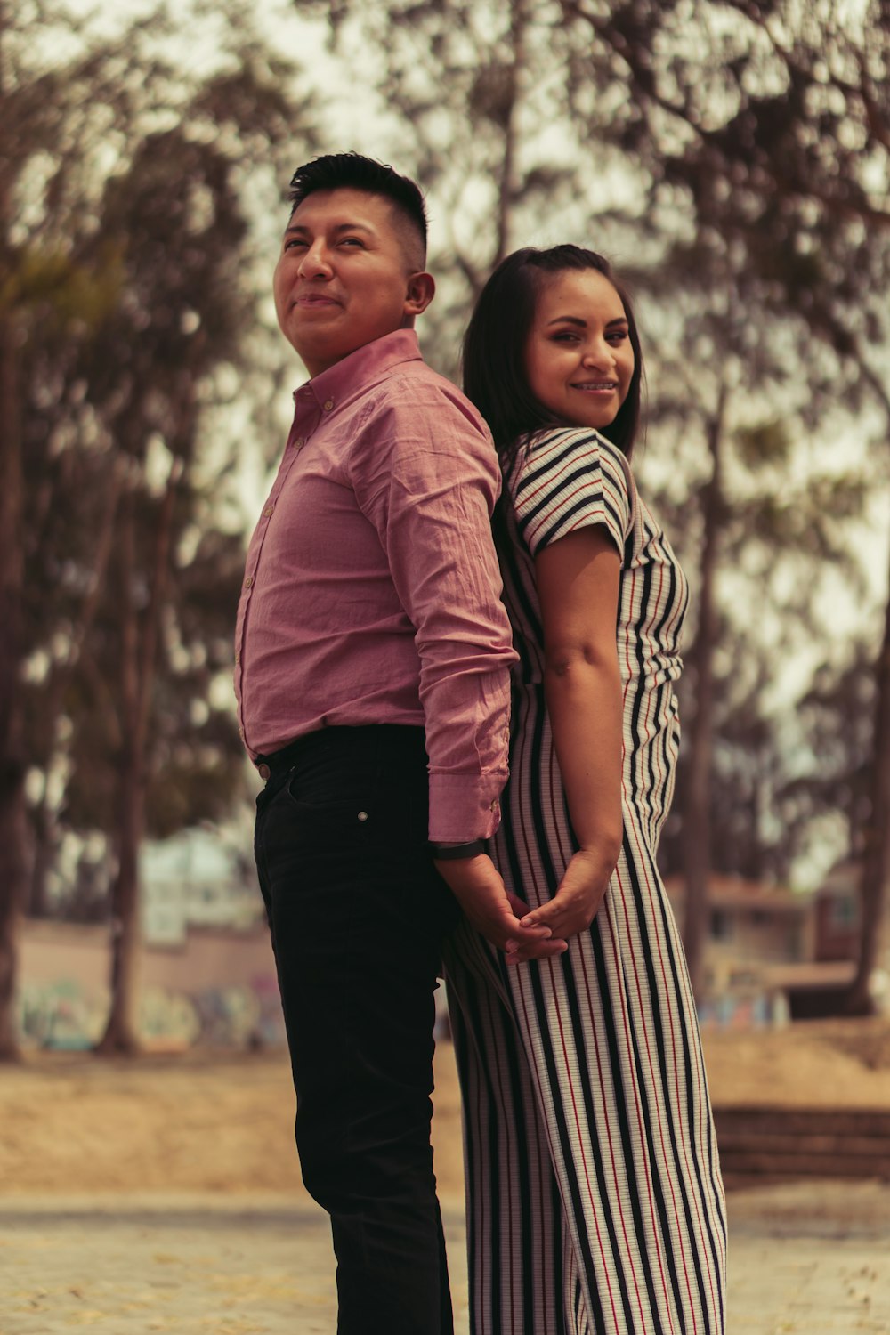 man in red dress shirt standing beside woman in black and white stripe dress