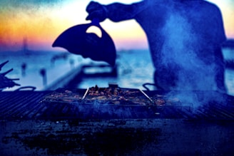 A sleek, black BBQ offset smoker with chrome accents, showcased outdoors with a sunset sky.