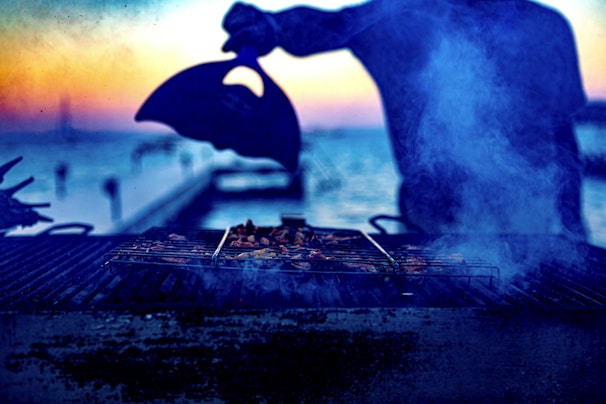 A hand-crafted BBQ offset smoker glowing warmly in a backyard setting during sunset.