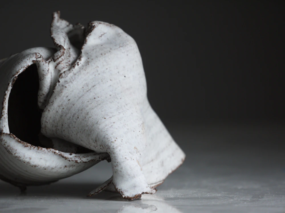 A folded, sculptural piece of white stoneware on a grey table