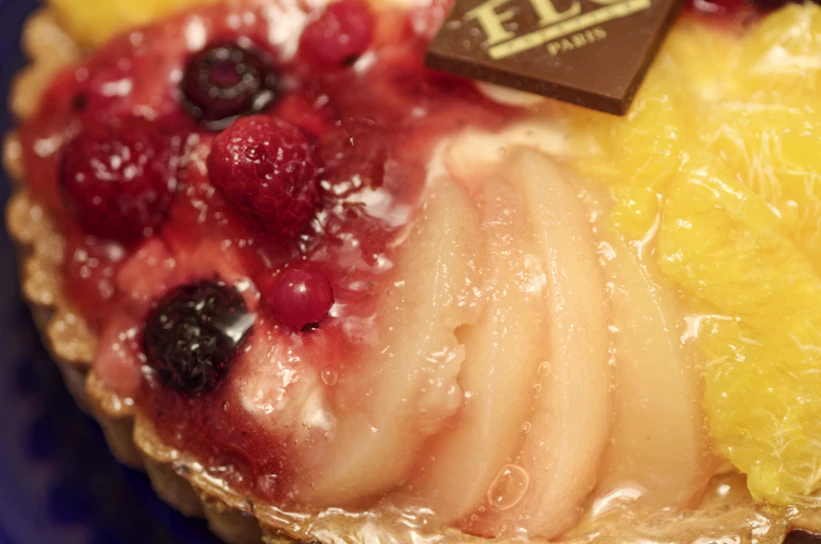 Close-up of a vibrant tropical fruit tart with glossy glaze and fresh mint leaves.