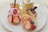 A variety of elegant desserts is arranged on a white plate. The selection includes pastries topped with strawberries, raspberries, blueberries, and apple slices. One dessert is adorned with pink whipped cream and a raspberry on top. In the background, a small glass contains an amber-colored drink.