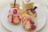 A variety of elegant desserts is arranged on a white plate. The selection includes pastries topped with strawberries, raspberries, blueberries, and apple slices. One dessert is adorned with pink whipped cream and a raspberry on top. In the background, a small glass contains an amber-colored drink.