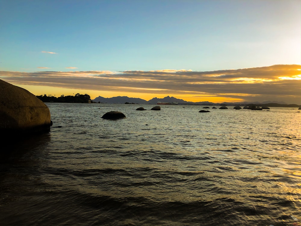 silhouette of rocks on sea during sunset