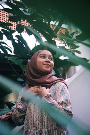 A serene outdoor portrait of a woman wearing a soft pastel skarf hijab, sunlight filtering through leaves behind her.