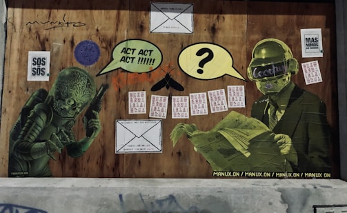 A wall covered with various street art elements, including two green humanoid figures. The figure on the left resembles a sci-fi alien with a large textured head, pointing towards something. The figure on the right is dressed in a suit and appears to be reading a newspaper, with a virtual reality visor displaying text. Speech bubbles with text like 'ACT ACT ACT!!!!!' and question marks hover above them. Numerous small flyers, an envelope drawing, and various graphic elements are pasted around them.