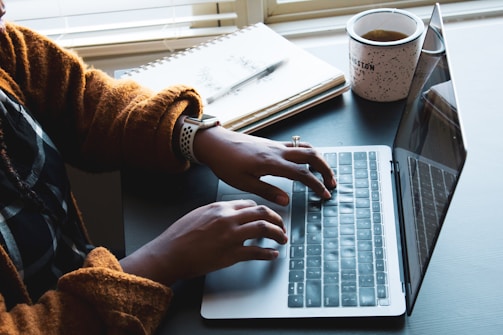 A person typing on a laptop in a cozy home office with a coffee mug nearby.