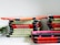 A stack of electronic tablets sits organized on a shelf, each in a protective case. The cases are predominantly red and green with a black trim, suggesting they may be used for educational or shared purposes.