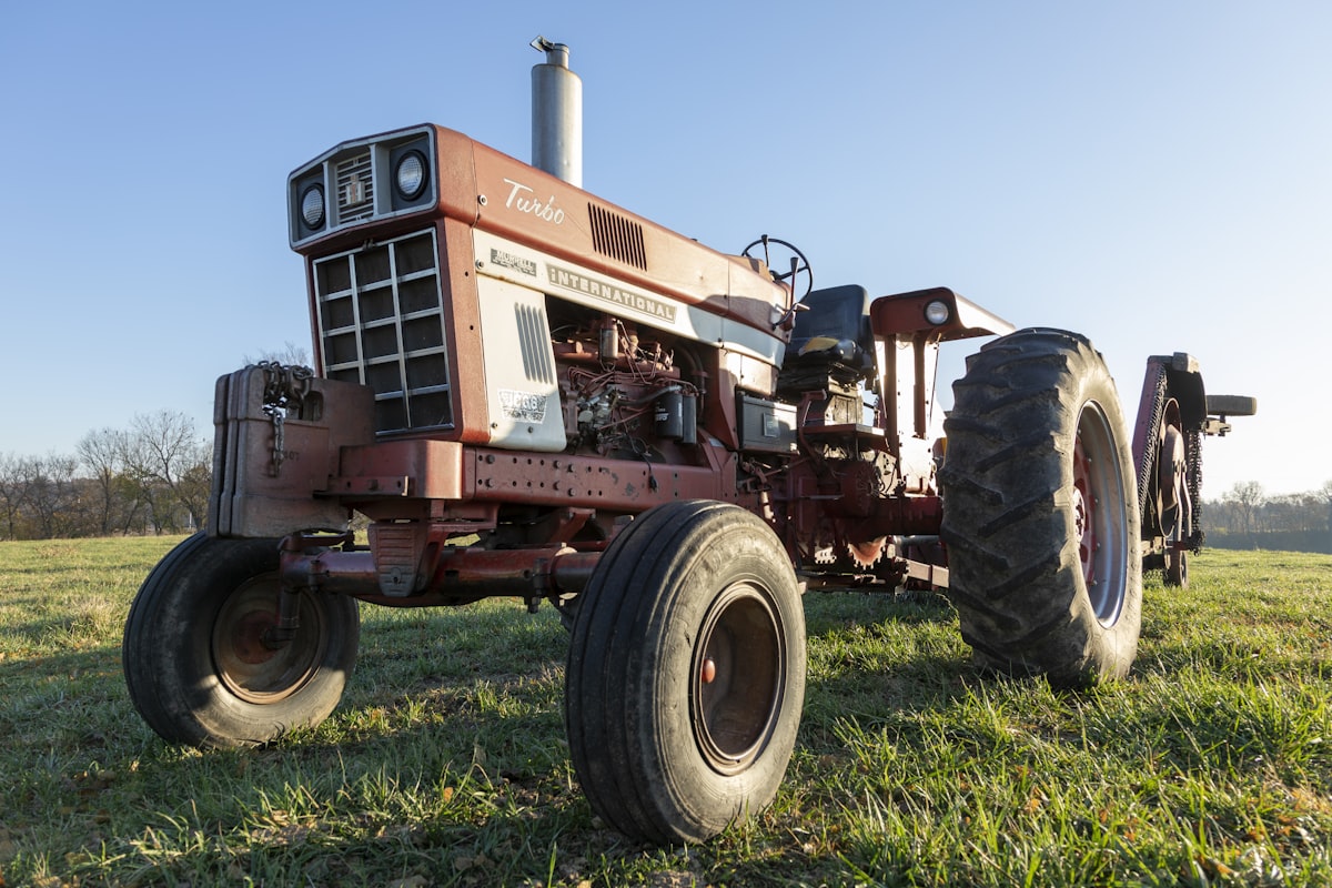 Red tractor on green grass field during daytime representing agricultural equipment and farming