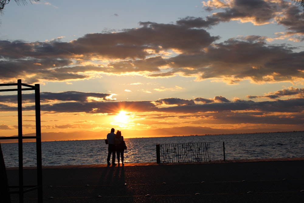 silhouette of 2 person standing on beach during sunset