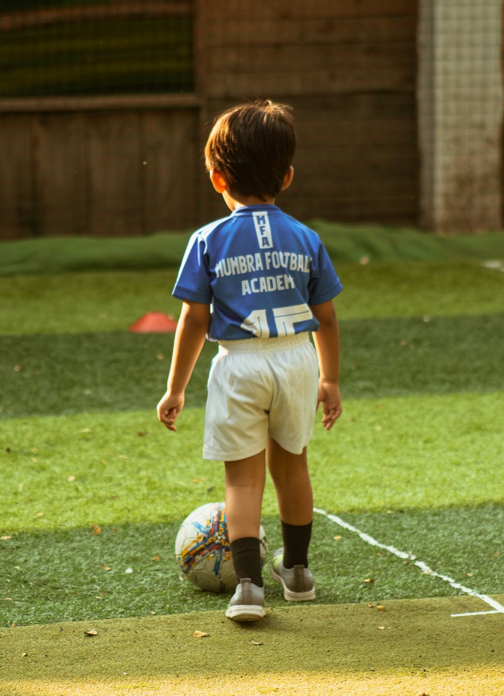 Chico con camiseta azul y blanca de cuello redondo y pantalones cortos marrones jugando al fútbol durante el día