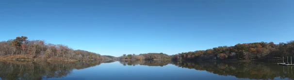 A serene nature documentary still capturing a calm lake surrounded by autumn trees.