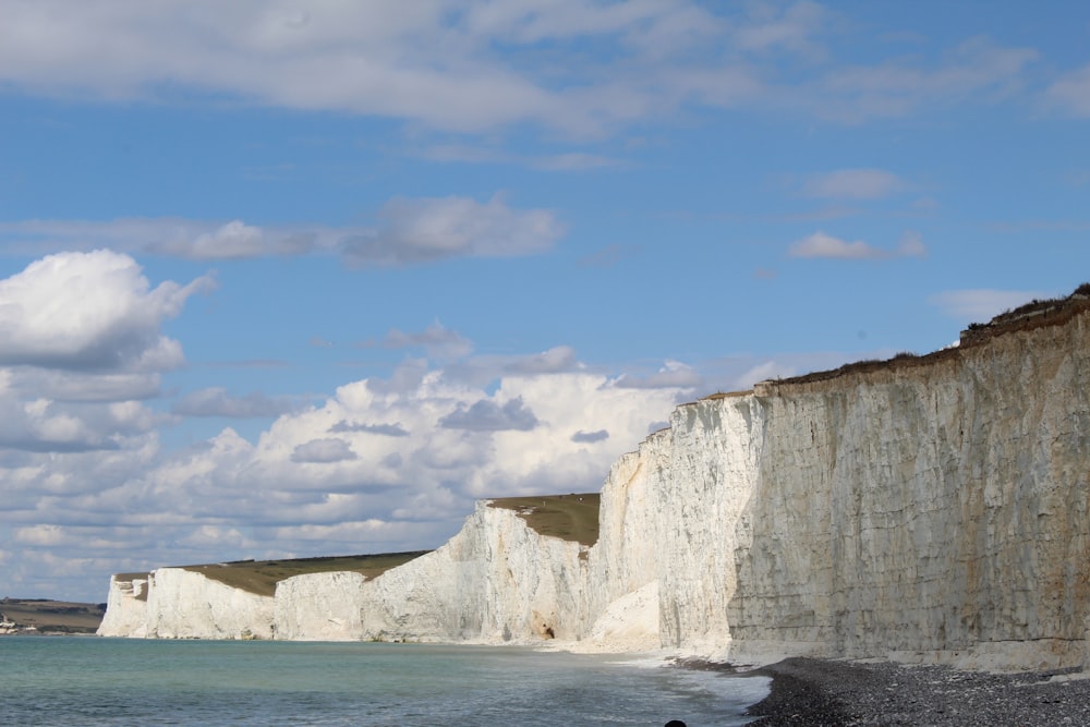 white and brown rocky mountain beside blue sea under blue and white cloudy sky during daytime