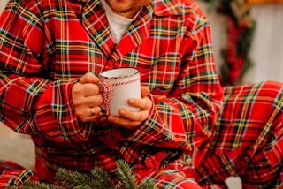 man in red and black plaid dress shirt holding white ceramic mug