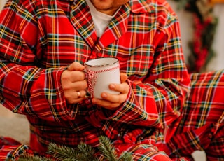 man in red and black plaid dress shirt holding white ceramic mug