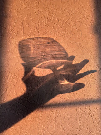 Subtle shadow of a circular sun symbol cast on a textured dusk-toned wall.