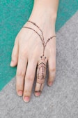 A hand adorned with intricate henna design and a delicate beaded chain, resting on a textured surface made up of green and gray sections.