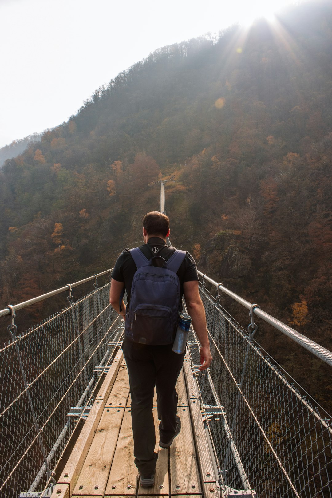 man in blue and black backpack walking on bridge during daytime